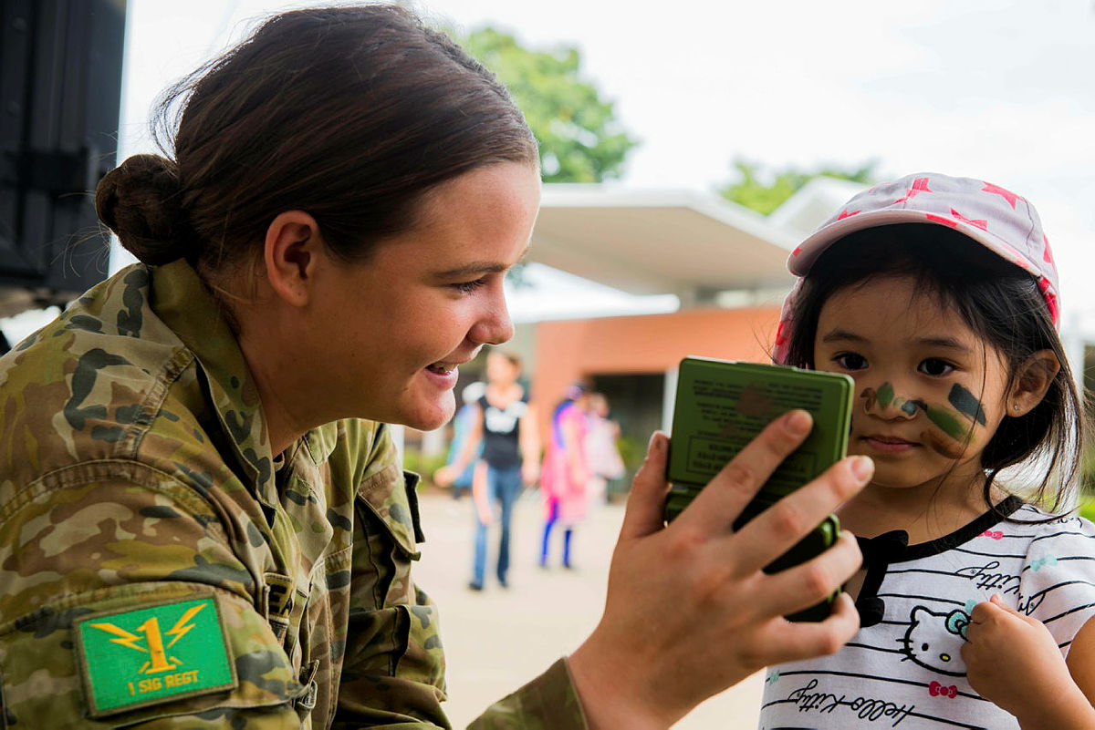 Australian Army soldier Private Bree-Anna Cheatham holds an Australian Army camouflage paint mirror to a girl during the Regis Aged Care Facility Community Day held on Wednesday 21st March 2018 in Salisbury, Brisbane QLD